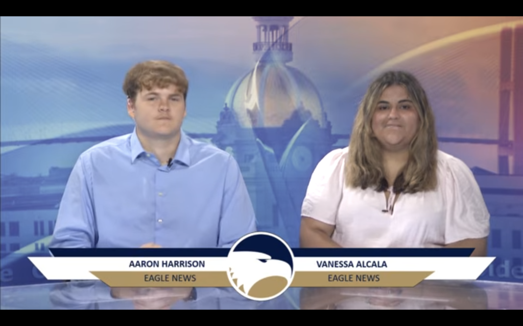 Aaron, wearing a blue shirt, and Vanessa, wearing a white shirt, sit at a news desk.
